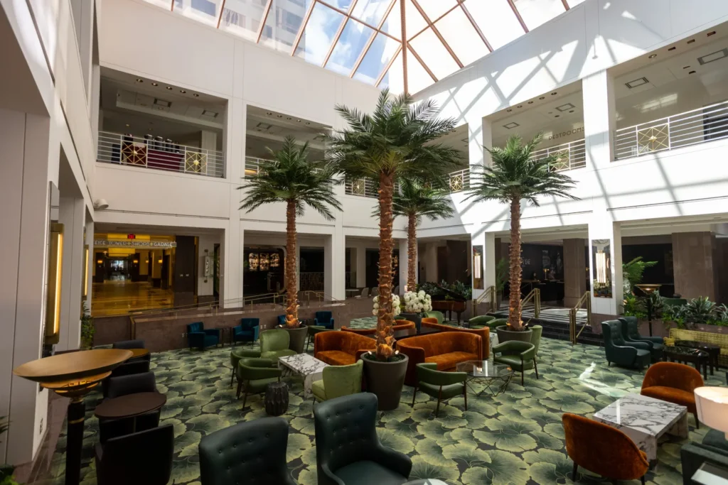 Bright hotel lobby atrium with a skylight, palm trees and lounge seating
